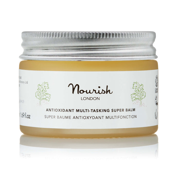 Nourish London Antioxidant Multi-Tasking Super Balm in a clear glass jar with silver lid, showing golden balm inside, labelled ‘Super Baume Antioxydant Multifonction’, on a white background