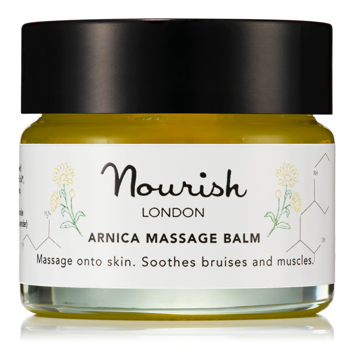 A clear glass jar of Nourish London Arnica Massage Balm with a black lid, displayed against a white background